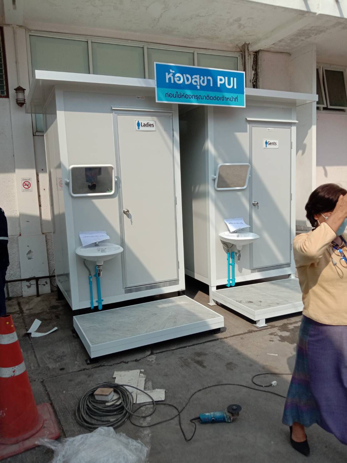 ห้องอาบน้ำสำเร็จรูปสีขาวแบบห้องคู่ ดีไซน์ทันสมัย ตั้งวางในพื้นที่ก่อสร้าง มุมมองด้านข้างเห็นโครงสร้างและประตูชัดเจน