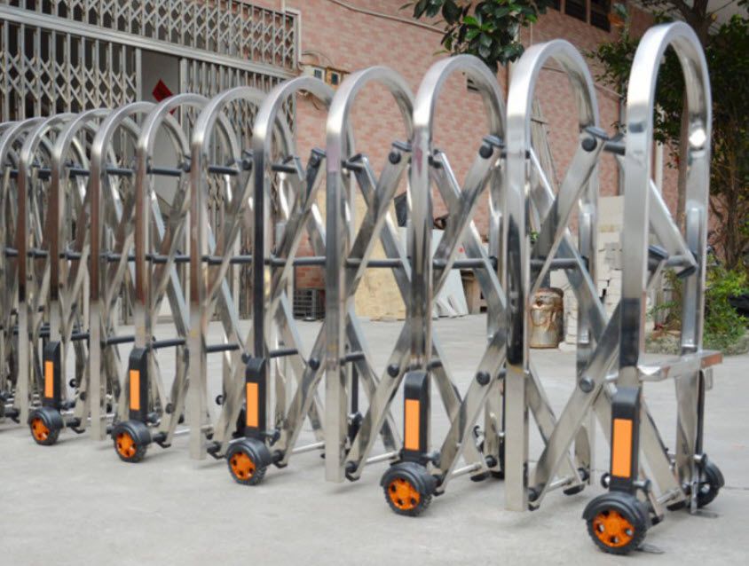 ประตูโฟลดิ้งเกท Folding Gate สีเงินสแตนเลสแบบพับได้ ติดตั้งบนพื้นราบพร้อมล้อเลื่อน มุมมองด้านข้างเห็นโครงสร้างเหล็กชัดเจน
