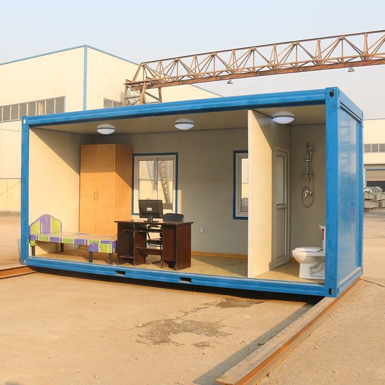 มุมมองด้านหน้าตู้ office สำนักงานสีน้ำเงินแบบคอนเทนเนอร์ ภายในจัดวางโต๊ะทำงานไม้สีเข้มและเก้าอี้สำนักงานพร้อมหน้าต่างกระจก
