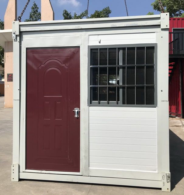 Container House แบบพับได้ (TEH-CH12) สีขาว ดีไซน์ทันสมัย ตั้งอยู่บนสนามหญ้า มุมมองเฉียงเห็นหน้าต่างเหล็กดัดและโครงสร้างตู้พับได้