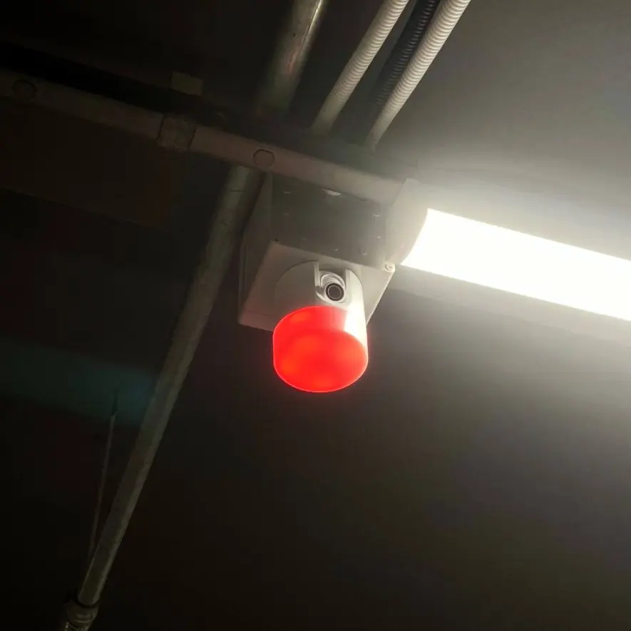 ตัวอย่างการติดตั้งกล้อง Video Parking Sensor บนเพดานลานจอดจริง ไฟสถานะสีแดงแสดงว่ามีรถจอด